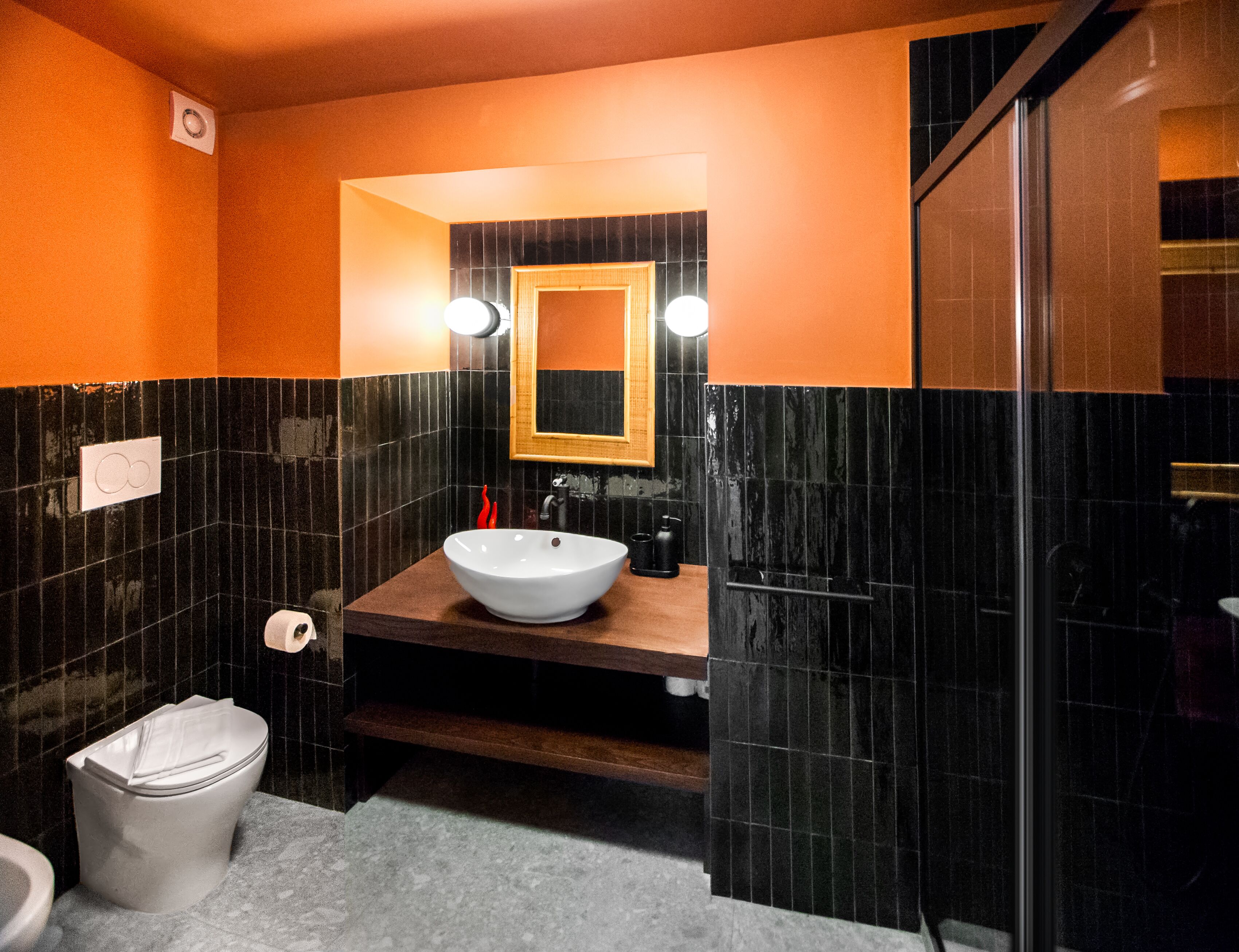 A bathroom with a white sink, black tiled walls, a wooden vanity, a mirror, and a toilet.