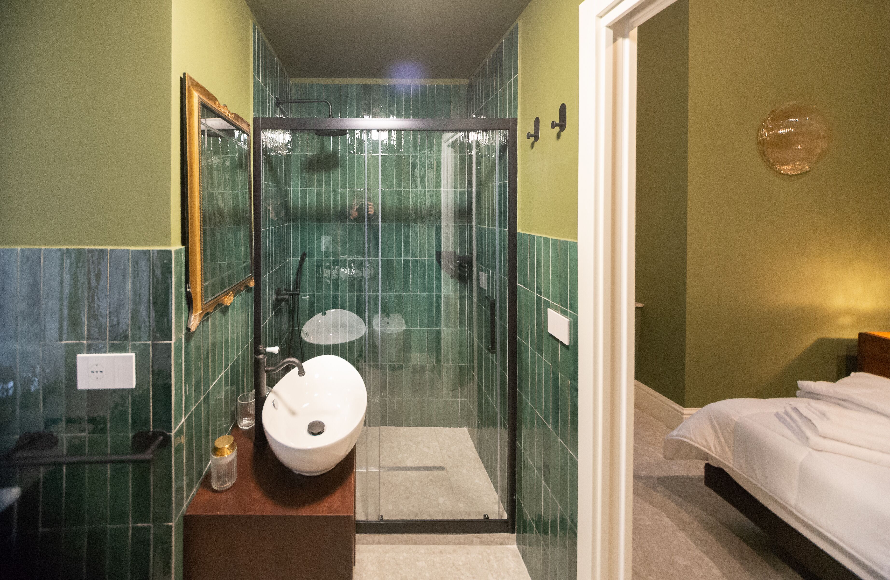 A bathroom with a glass-enclosed shower, a sink, and a bed.