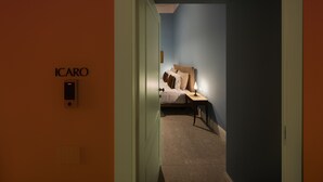 A hallway leading to a bedroom with a bed, a nightstand, and a wall-mounted light. The room has blue walls and a carpeted floor. - Monart Hospitality Capodimonte (Naples)
