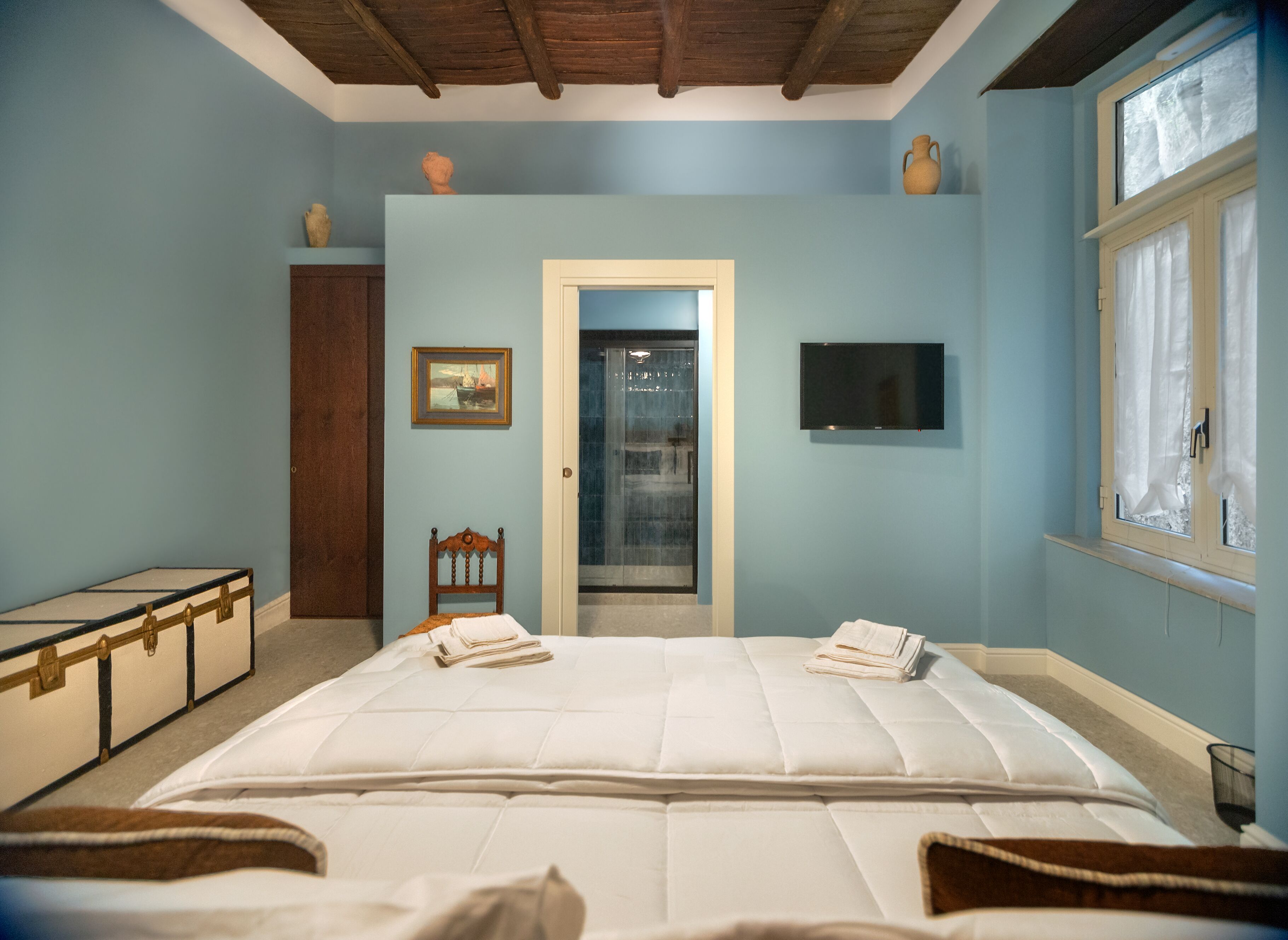 A bedroom with a large bed, a wooden chair, a television, and a window with curtains.