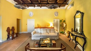 A living room with a sofa, coffee table, and a mirror. There are two doors, a lamp, and a decorative vase. - Monart Hospitality Capodimonte (Naples)