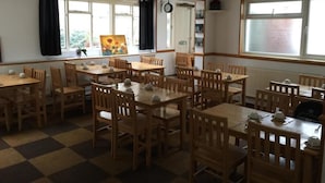 A dining area with multiple wooden tables and chairs, a checkered floor, and large windows with curtains. - Hellenic Hotel London by Saba (London)
