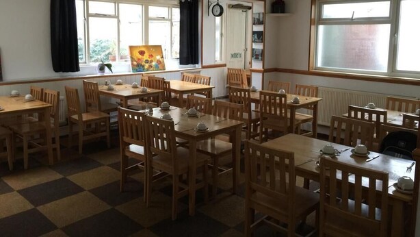 A dining area with multiple wooden tables and chairs, a checkered floor, and large windows with curtains. - Hellenic Hotel London by Saba (London)