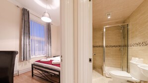A hotel room with a bed, a window with curtains, a shower area with a glass door, and a toilet. - Hellenic Hotel London by Saba (London)