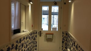 A hallway with a white door, floral wallpaper, and a fire extinguisher mounted on the wall. - Hellenic Hotel London by Saba (London)