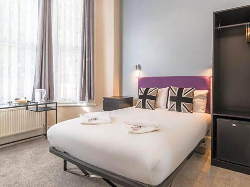 A neatly made bed with pillows, a bedside table with a lamp, and a window with curtains.