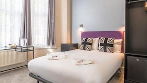 A neatly made bed with pillows, a bedside table with a lamp, and a window with curtains. - Hellenic Hotel London by Saba (London)