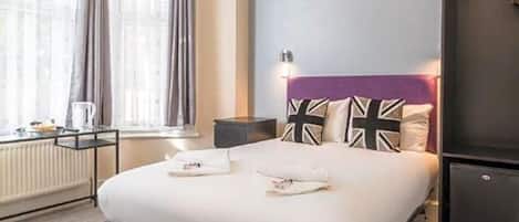 A neatly made bed with pillows, a bedside table with a lamp, and a window with curtains.