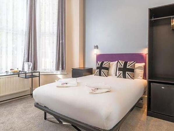 A neatly made bed with pillows, a bedside table with a lamp, and a window with curtains.