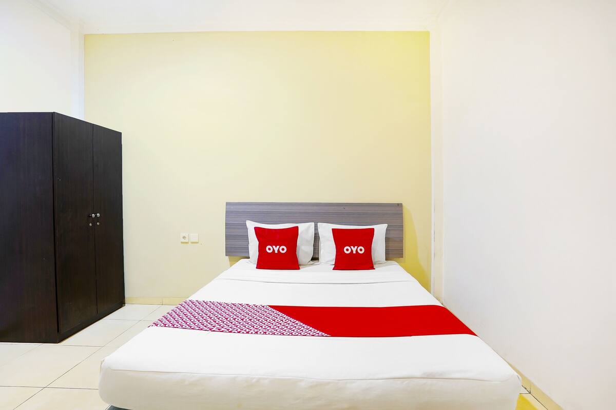 A hotel room with a bed, a wardrobe, and a plain wall.