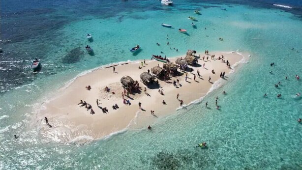 An aerial view of a beach with clear turquoise waters, several boats, and people enjoying the beach and water. - Villa Cruz Hotel & Restaurant Windsurf Fan Eco Rm (buen hombre)