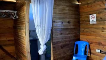 Eine rustikale Holzjagdhaus mit einem einzigen Raum, ausgestattet mit einem Bett, einem blauen Stuhl und einem Duschbereich.