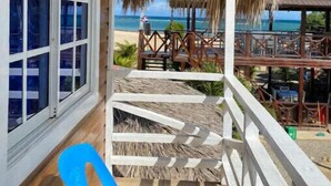 A wooden deck with a thatched roof, a blue chair, and a view of the beach and ocean. - Villa Cruz Hotel & Restaurant Windsurf Fan Eco Rm (buen hombre)