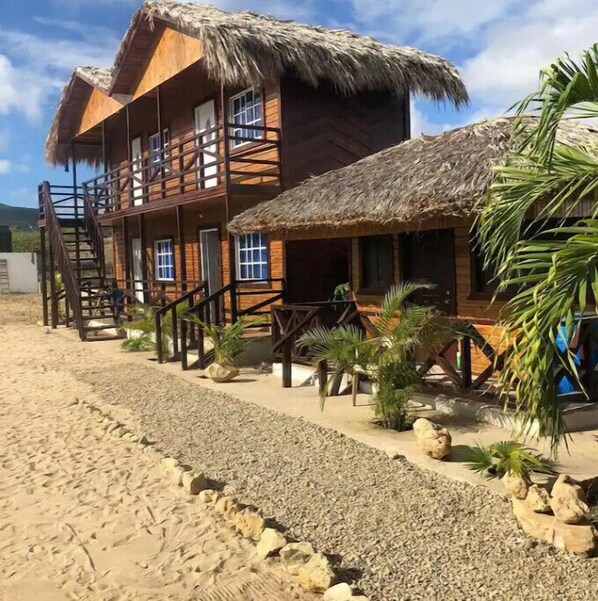 Un edificio de madera con techo de paja, varios balcones y una playa arenosa al frente.