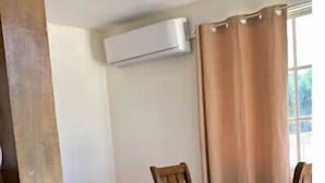 Un comedor con mesa y sillas de madera, un sofá rojo y un ventanal con cortinas.
