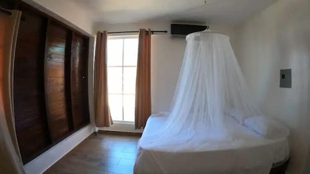 Un dormitorio con cama, ventana con cortinas y un armario de madera.