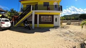 A two-story building with a yellow facade, a staircase leading to the upper floor, and a car parked in front. - Villa Cruz Hotel & Restaurant Ocean View (buen hombre)