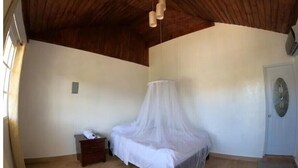 Un dormitorio con techo de madera, una cama con dosel blanco, una mesita de noche, una puerta y una ventana.