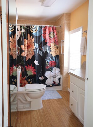 A bathroom with a toilet, a shower curtain with floral patterns, a towel rack, and a sink with a countertop. - The Boutique Lagoon House (Fort Pierce)