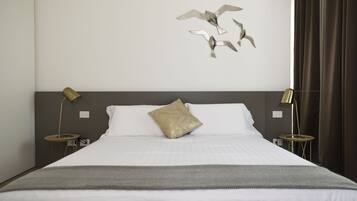 Una cama bien hecha con un cojín decorativo, dos mesitas de noche con lámparas y una obra de arte en la pared con aves.