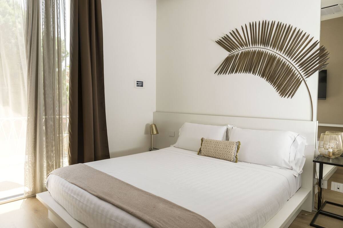 A neatly made bed with white linens, a decorative wall piece, and a bedside table with a lamp.