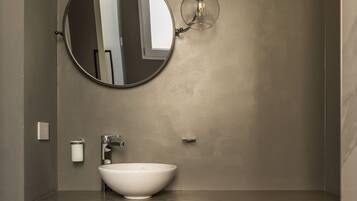 A modern bathroom with a round mirror, a white sink, a towel rack, and a small storage cabinet.