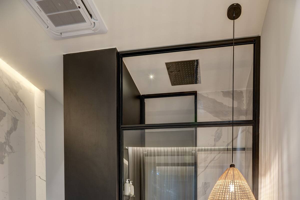 A modern bedroom with a large bed, a glass shower enclosure, a hanging light fixture, and a small potted plant.