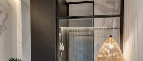 Un dormitorio moderno con una cama grande, cabina de ducha de vidrio, lámpara colgante y una pequeña planta en maceta.