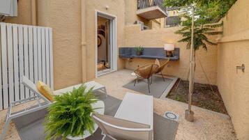 Eine kleine Terrasse im Freien mit einem weißen Tisch, zwei Stühlen, einem Blumentopf und einer hängenden Lampe.