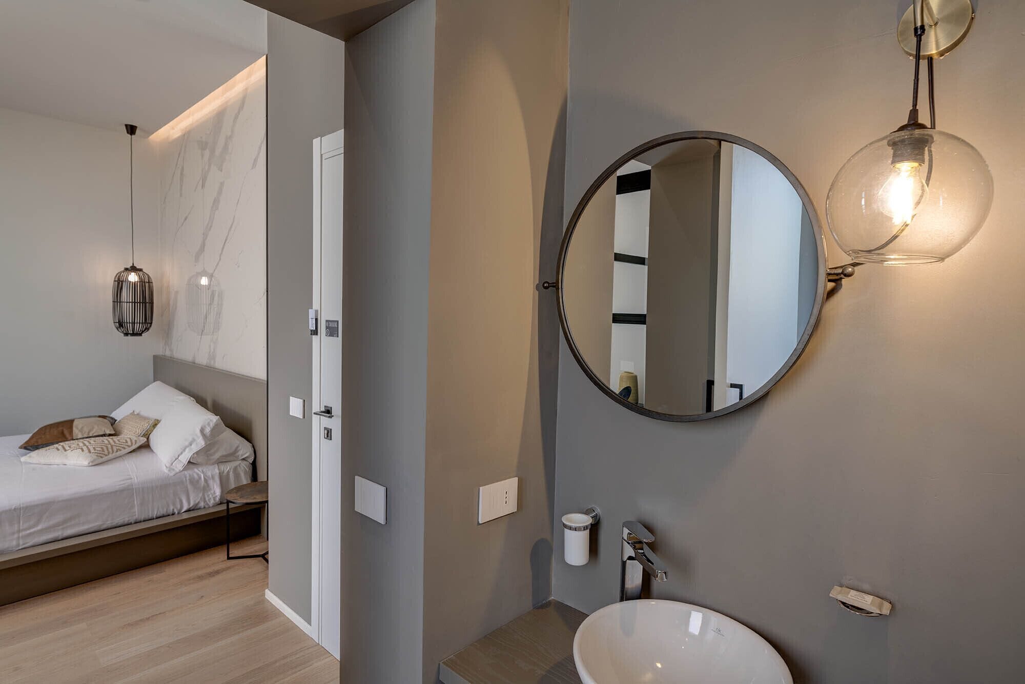 A modern bedroom with a bed, bedside table, and a round mirror with a light fixture.