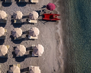 An aerial view of a beach with multiple umbrellas and beach chairs arranged in rows. - Le Palmette Suites (Cagliari)
