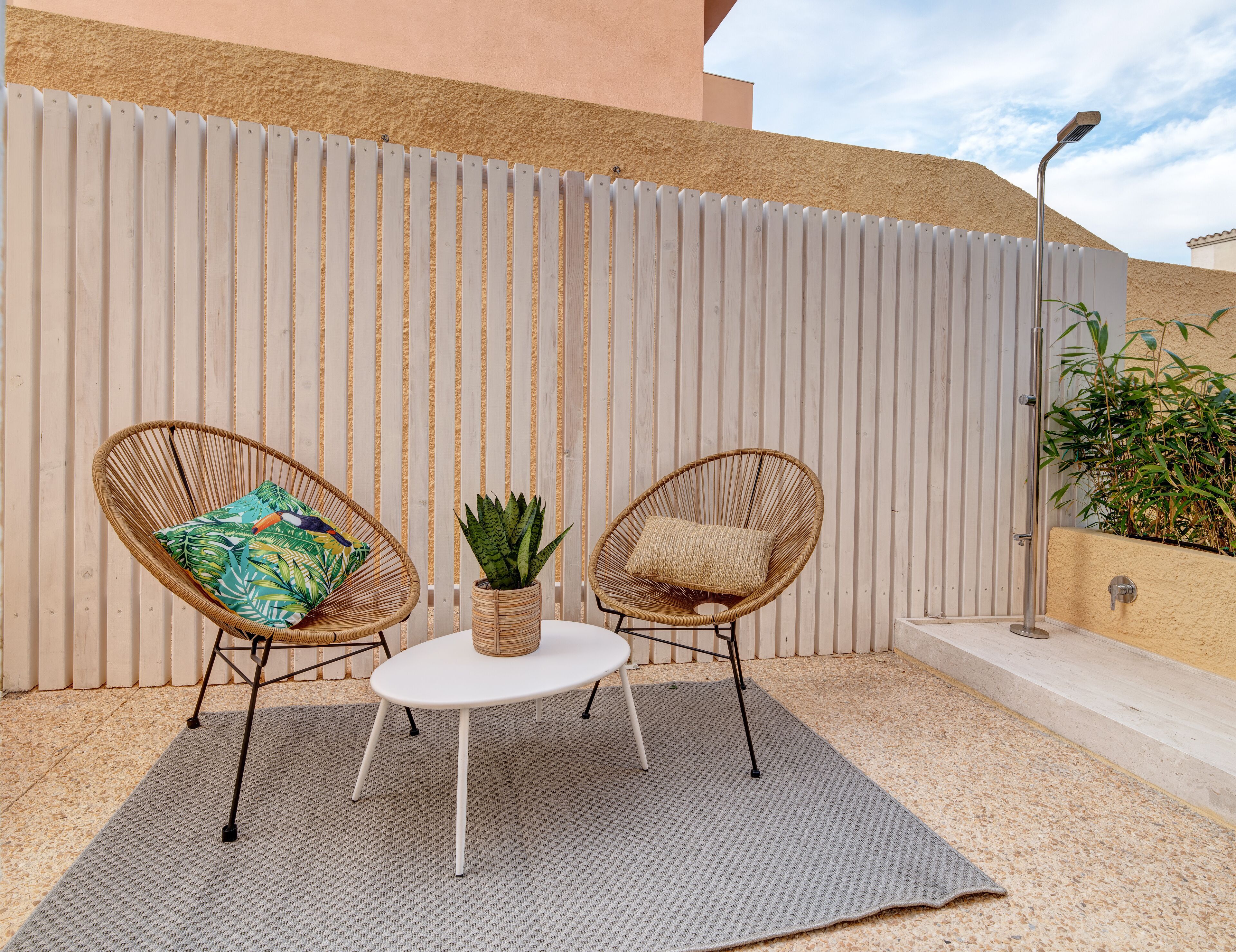 Un patio con dos sillas de mimbre, una mesa redonda pequeña y una planta en maceta.