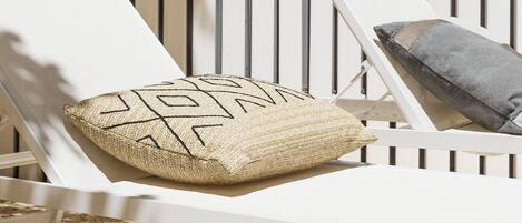 A white sun lounger with a woven pillow and a cushion, positioned against a vertical wooden panel wall.