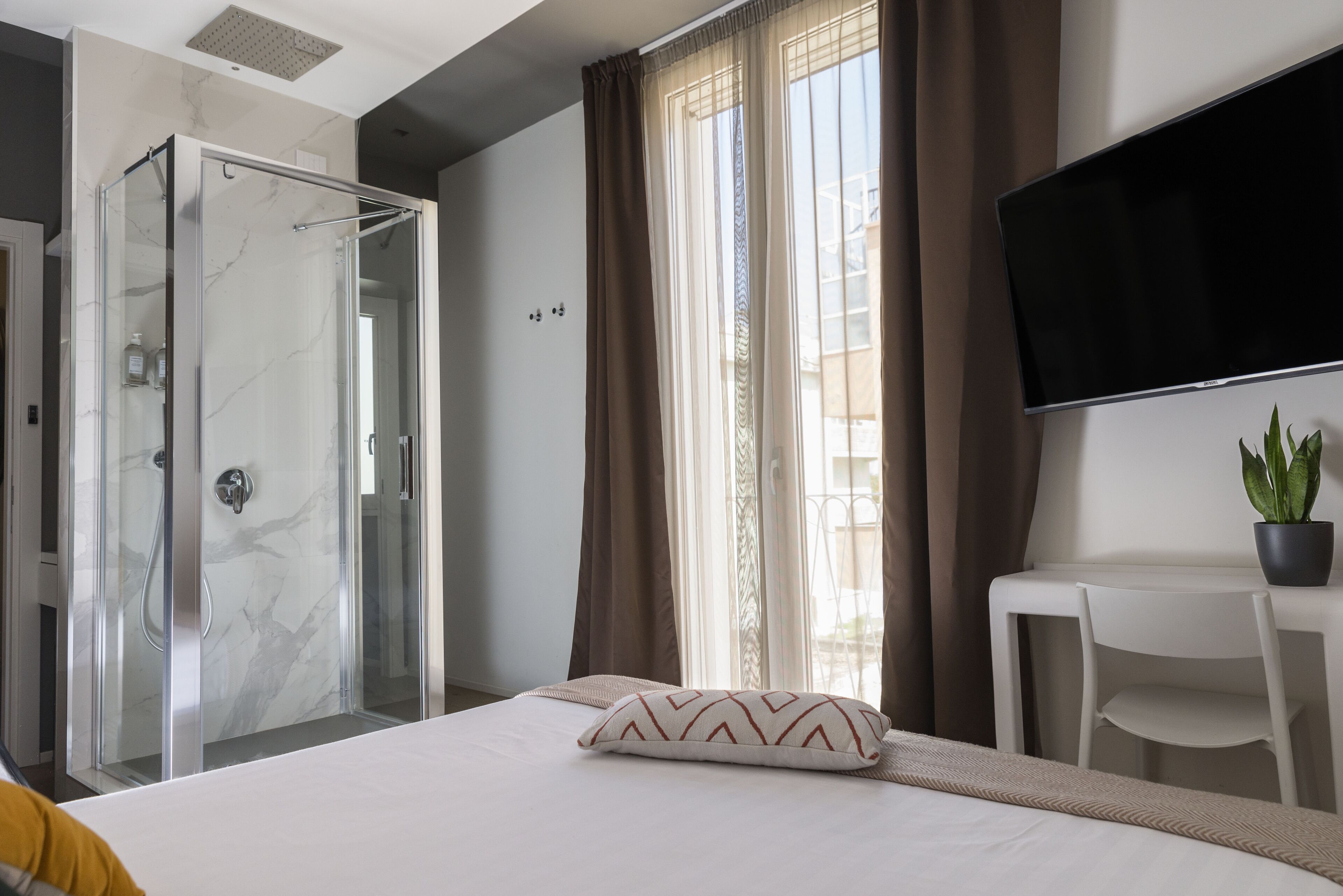 Habitación de hotel con cama, escritorio, televisión, ducha y planta en maceta.