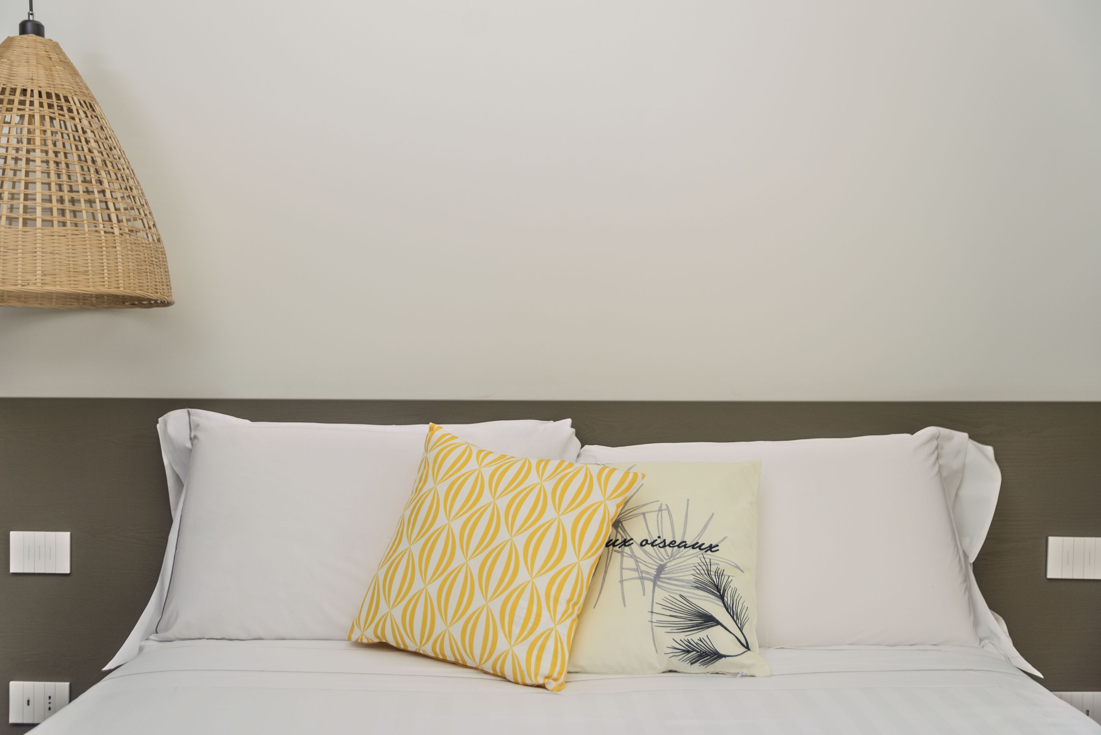 A bed with white bedding, a yellow patterned pillow, and a white pillow with a palm leaf design.