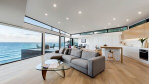 A modern living room with a glass coffee table, a grey sofa, and a view of the ocean. - Sea Ranch | Popular Coastal Retreat with Ocean View Bath (Wye River)