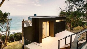 A modern, minimalist house with a large glass door, situated on a hillside overlooking the ocean. - Sea Ranch | Popular Coastal Retreat with Ocean View Bath (Wye River)