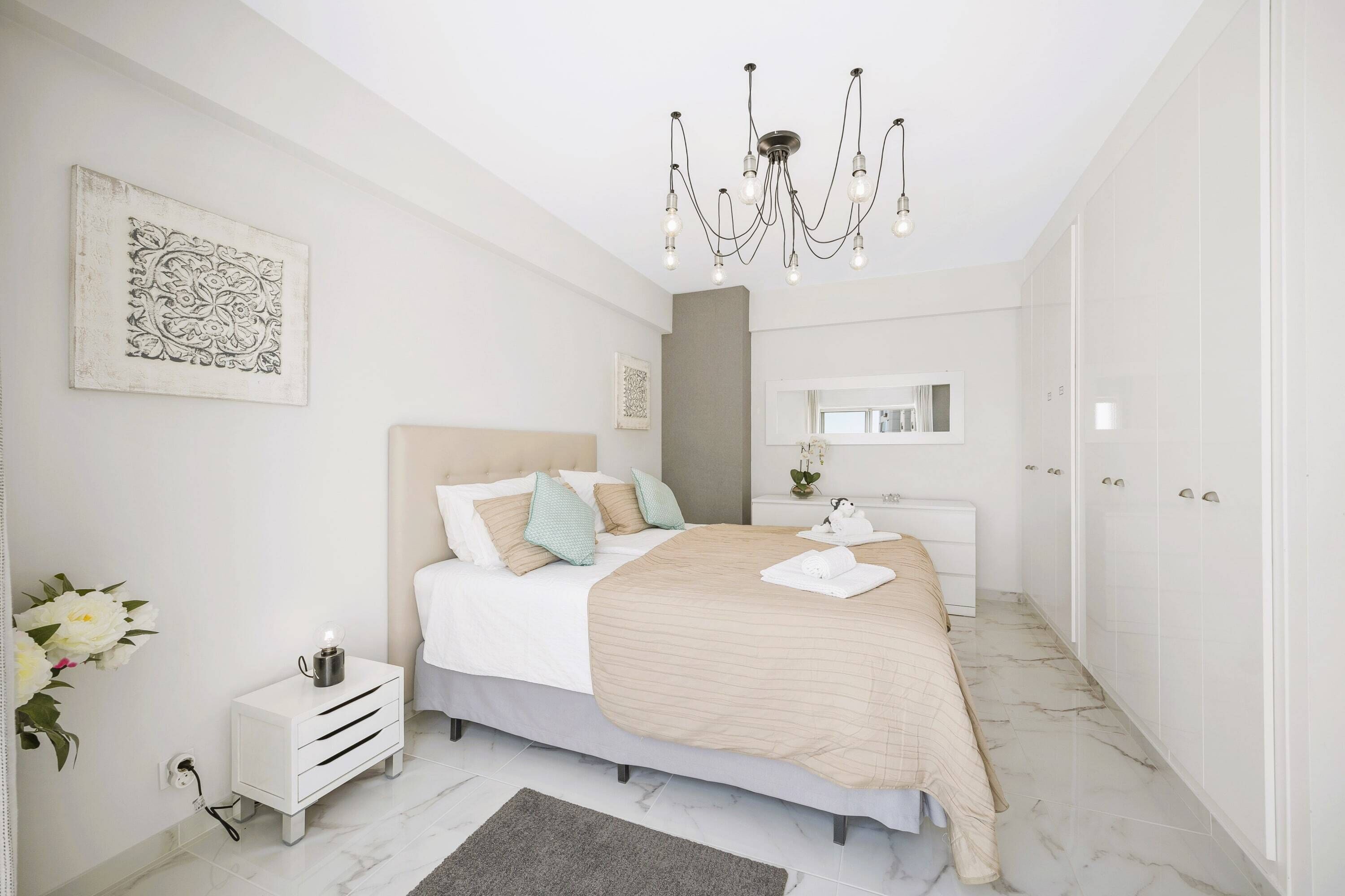 Une chambre à coucher moderne avec un grand lit, des tables de chevet, un lustre et une salle de bain équipée d’un miroir et de toilettes.