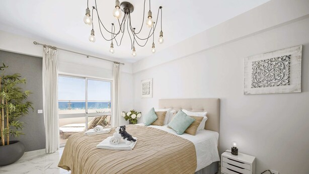 Ein Schlafzimmer mit einem Bett, einem Nachttisch, einer Topfpflanze, einem Fenster mit Blick und einer Chandelier.