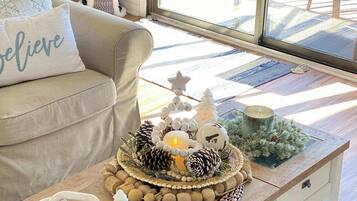Un salon chaleureux avec un canapé, une table basse agrémentée d’un élément décoratif, et une vue sur l’extérieur grâce à de grandes fenêtres.