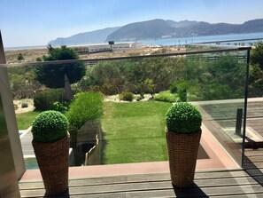 Uma varanda com vista para uma praia, uma área gramada e uma montanha ao longe.