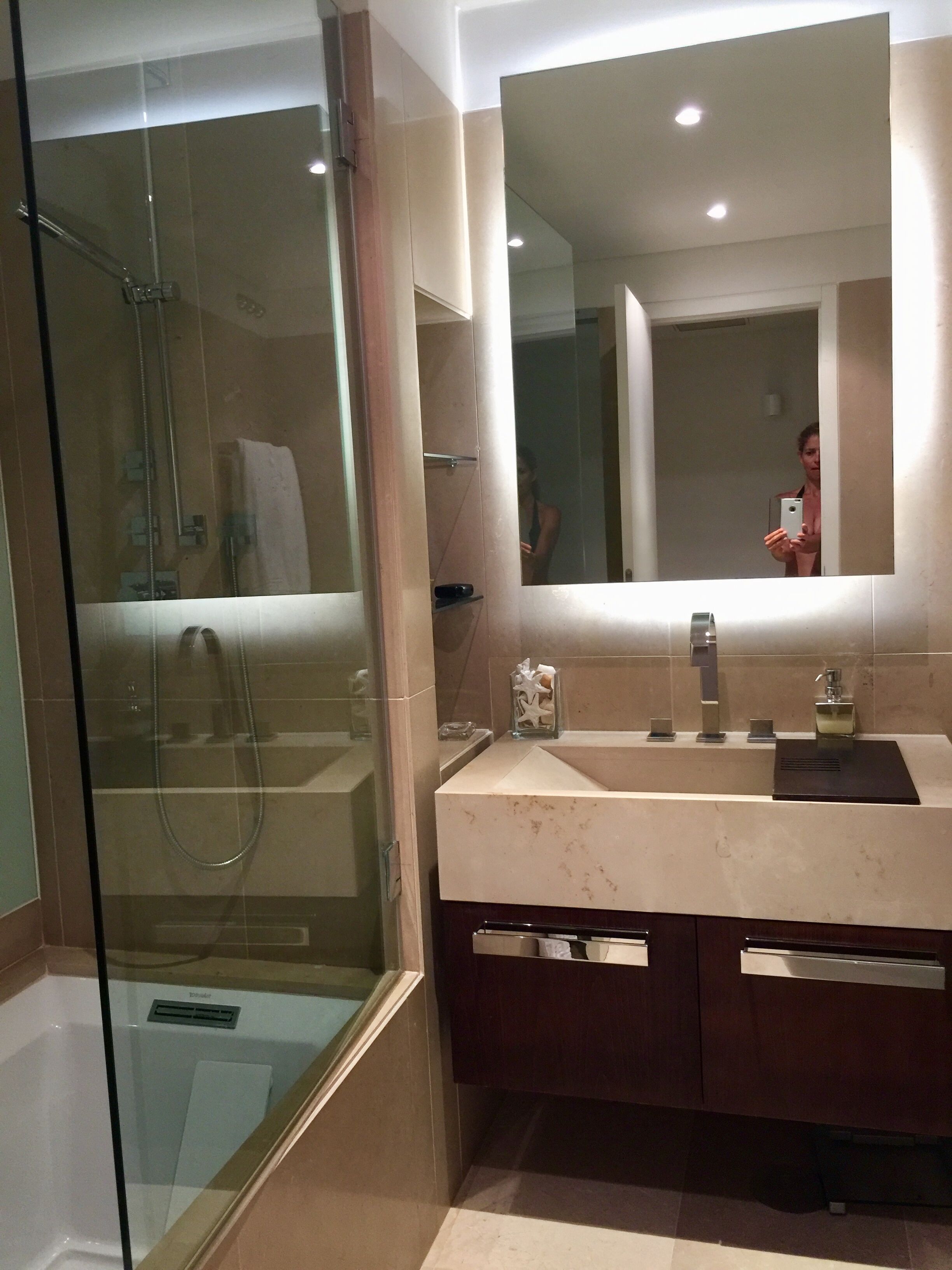 Une salle de bain moderne avec une douche à parois de verre, un grand miroir et un meuble-lavabo en marbre.