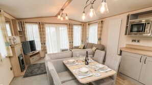 Una habitación acogedora y bien iluminada con una mesa de comedor para cuatro personas, un sofá, un televisor y una kitchenette con microondas.