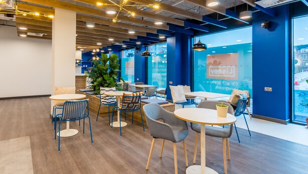 Een moderne kantoorruimte met ronde tafels, blauwe stoelen en een grote plant.