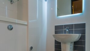 Een moderne badkamer met een wit toilet, een glazen douchecabine, een wastafel met een spiegel erboven en zwart betegelde wanden.