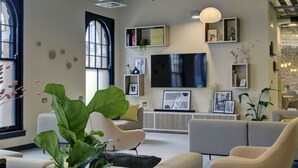 Een moderne woonkamer met een grote televisie, comfortabele zithoek en decoratieve planten.