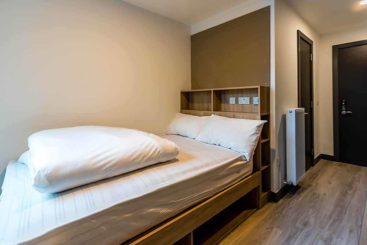 Ein Einzelbett mit weißer Bettwäsche, einem Holzkopfstück und einer eingebauten Regalwand.