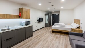Een moderne hotelkamer met kitchenette, een bed met houten hoofdeinde en een grijze bank.