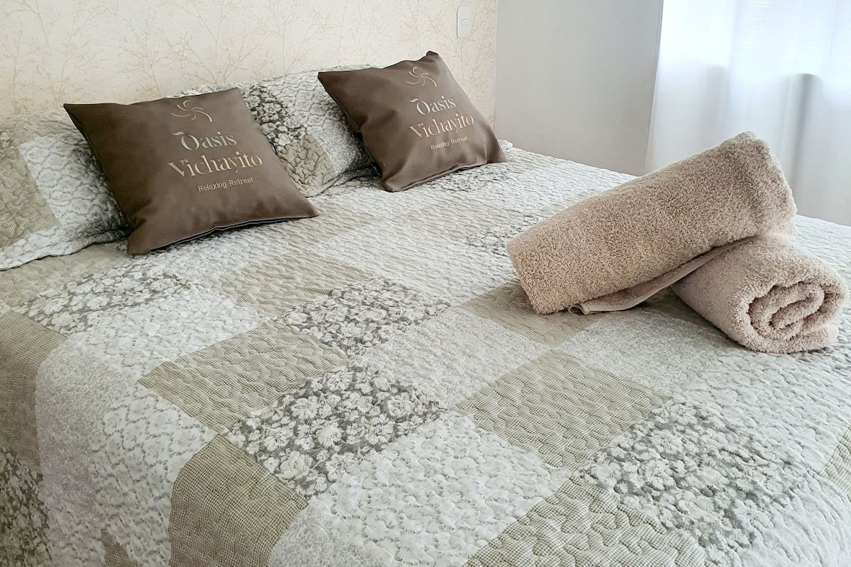 A neatly made bed with a quilt, two brown pillows, and a rolled towel.
