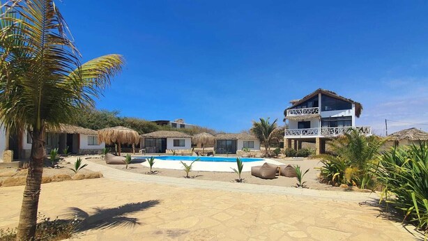 Resort com piscina, bangalôs de palha e um prédio de dois andares com varanda.